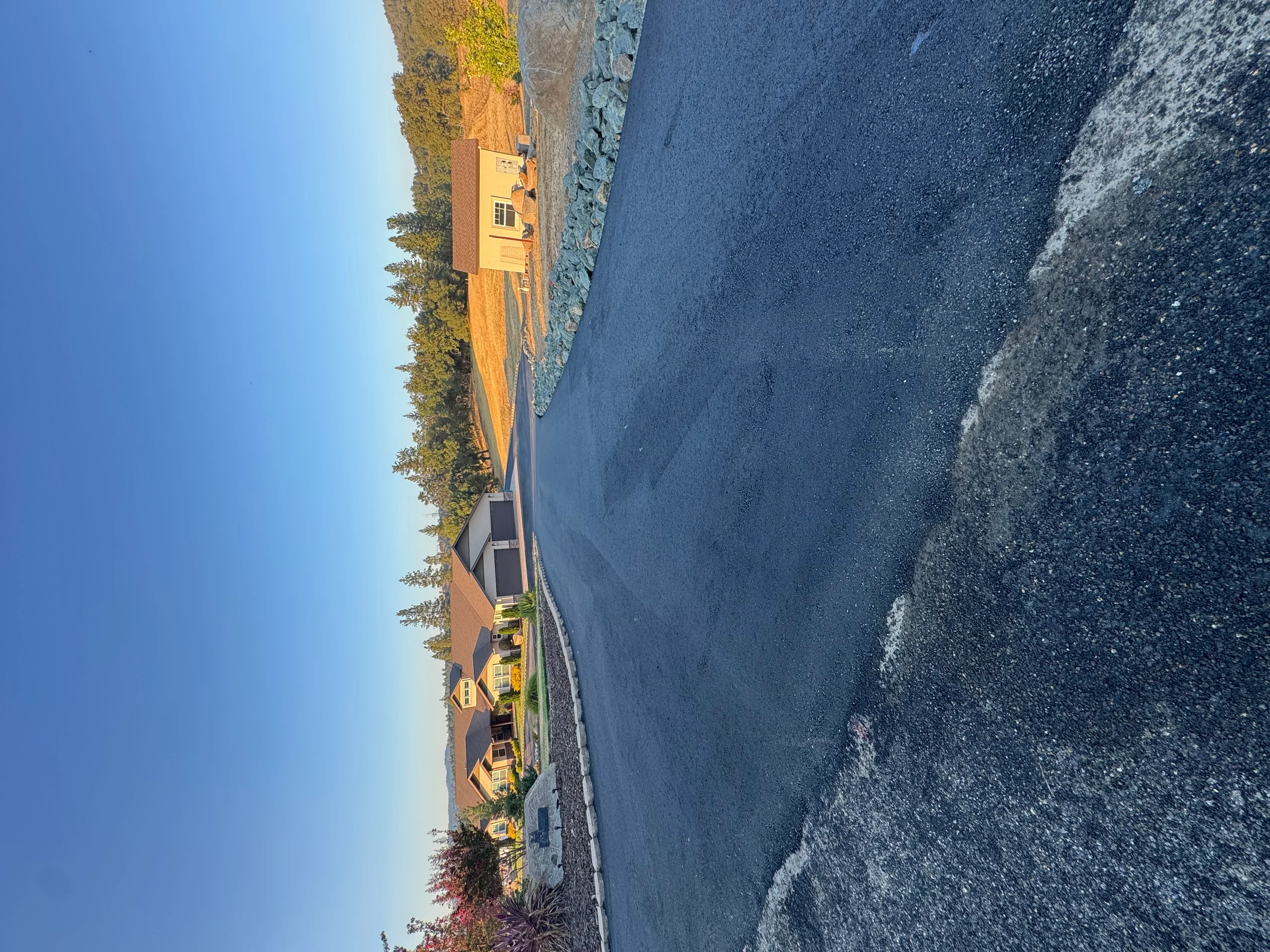 Newly paved black asphalt driveway at residential home with yellow exterior