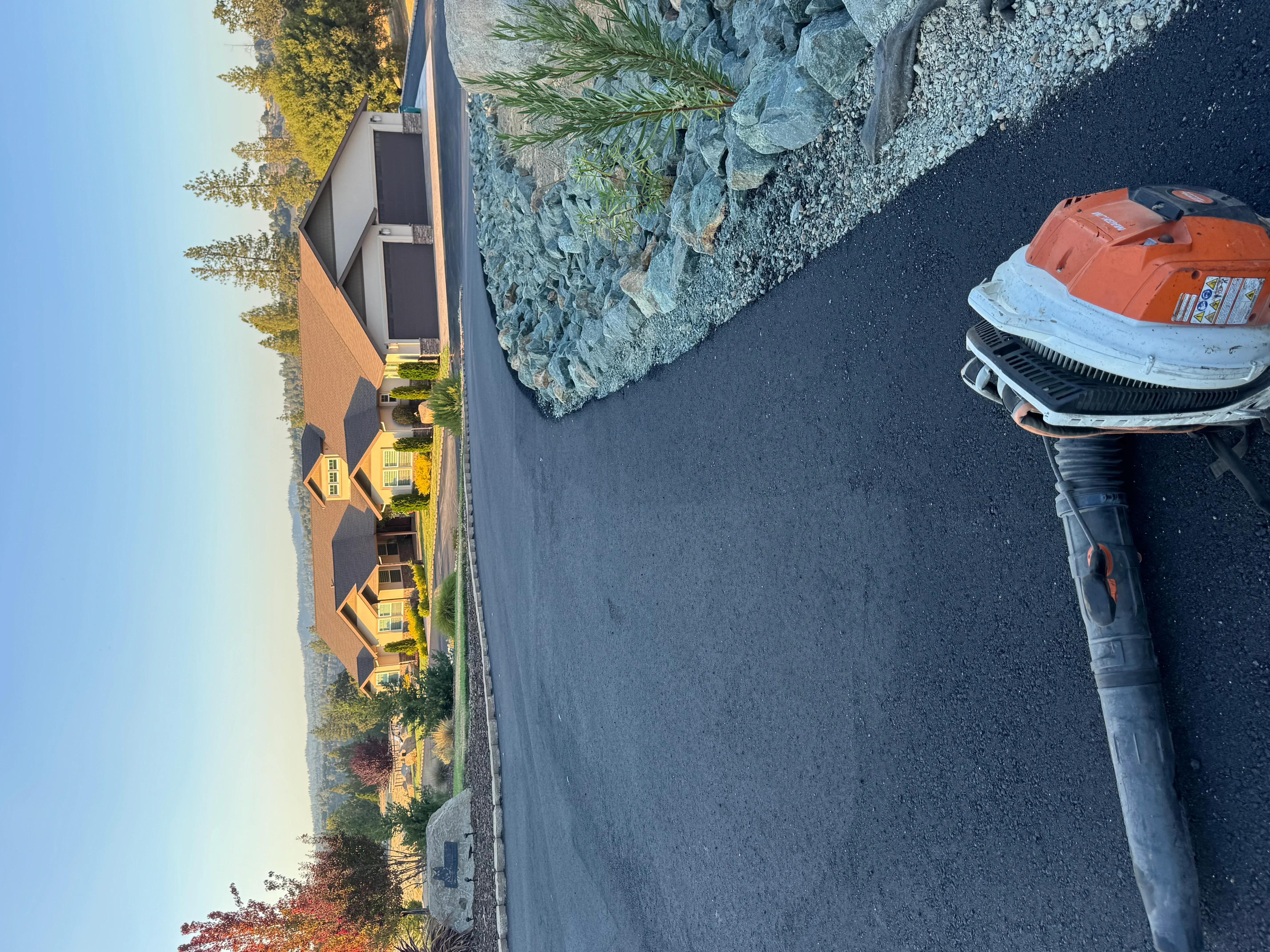 Newly paved black asphalt driveway beside brick residential home in Valley Springs